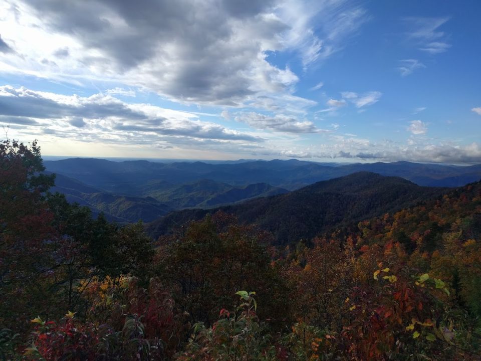 Mountain range with clouds in the sky. Some trees in the foreground have fall colors