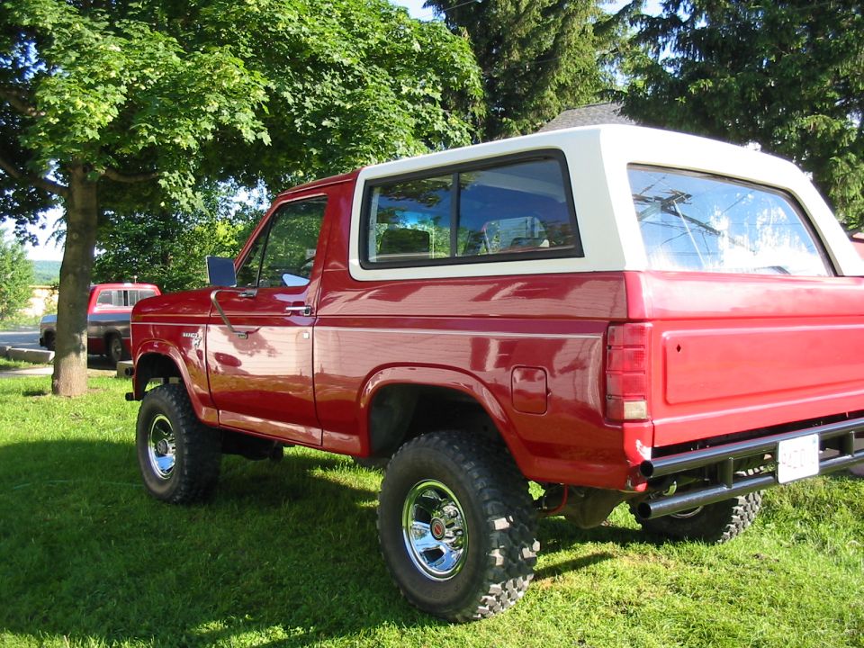 Red Ford Bronco with a white removable top, lifted suspension, and chrome wheels parked on grass