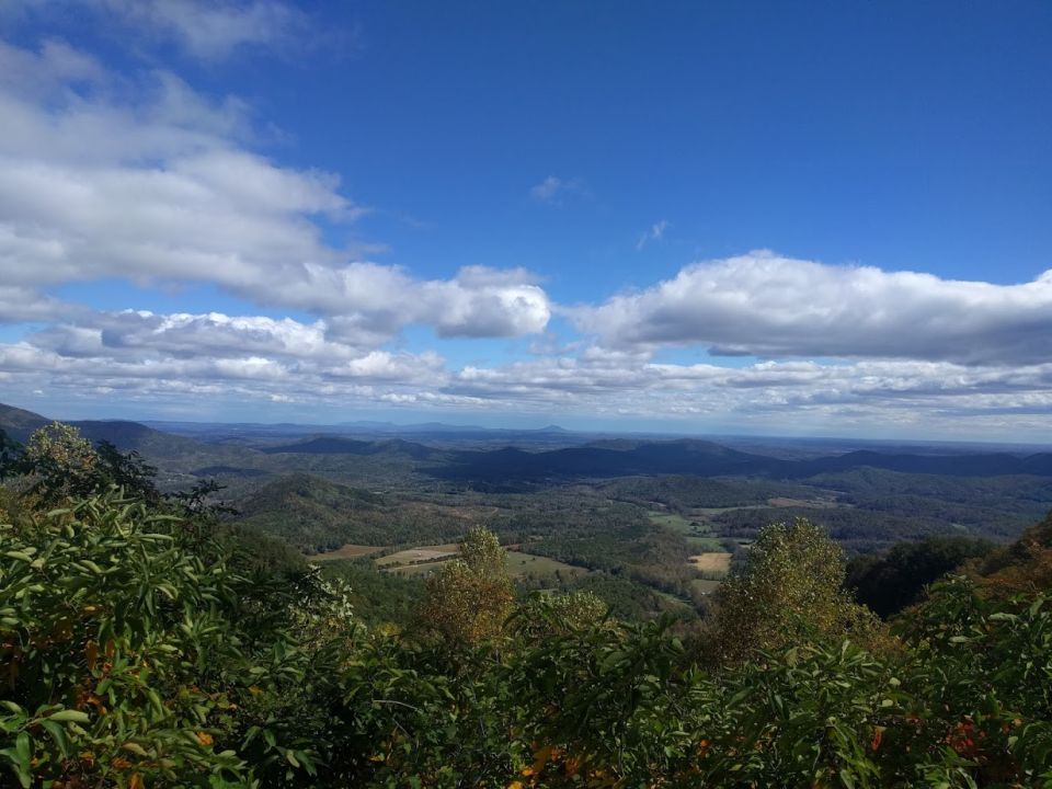 Mountainous terrain under a blue sky with scattered clouds. Foreground shows green foliage