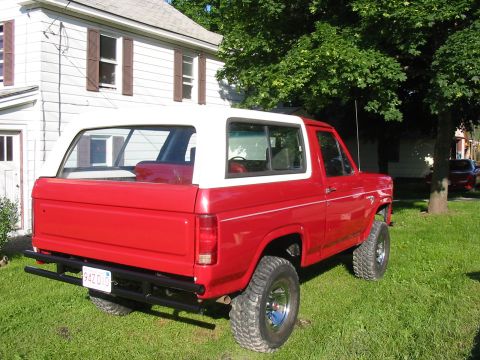 1981 Ford Bronco - Rear view of a lifted 1980 Ford Bronco with a white top parked on grass next to a house.