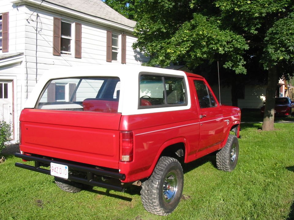 Red 1980 Ford Bronco with white removable top, lifted suspension, and aftermarket rear bumper. License plate reads PAZ 010