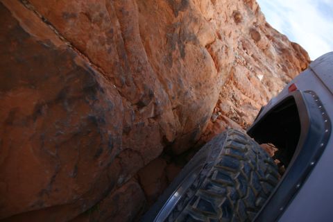 1979 Ford Bronco - A close-up view of a tire and fender of a vehicle navigating a narrow passage between large red rock formations.