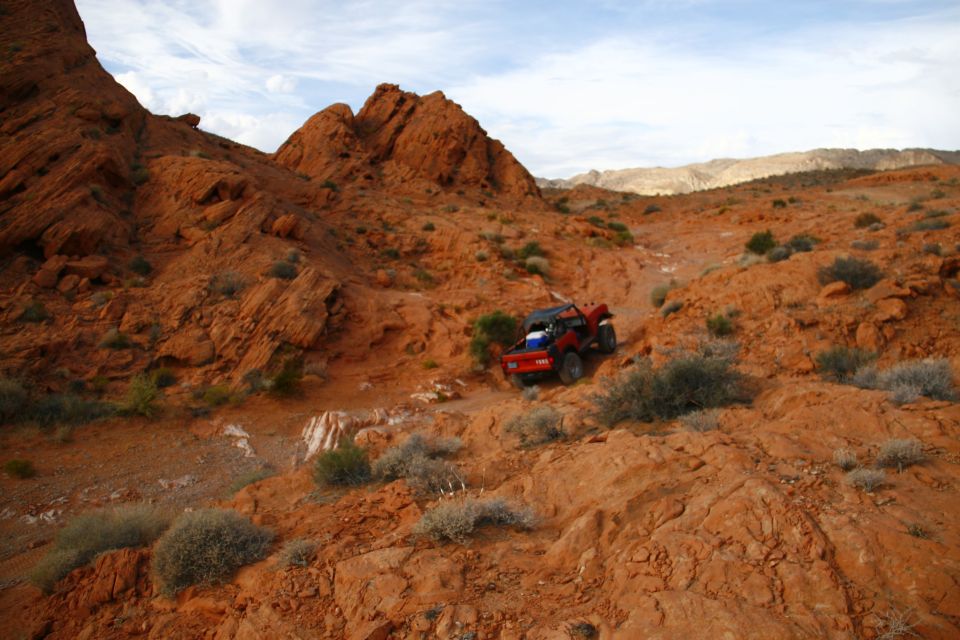 Red off-road vehicle driving on a rocky desert trail.