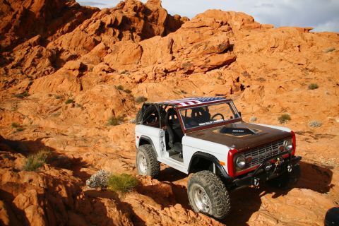 1979 Ford Bronco - A white 1979 Ford Bronco with an American flag-themed roof is parked on a rocky, orange desert landscape.