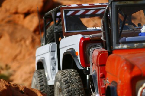 1979 Ford Bronco - Two off-road RC vehicles are parked side-by-side in a desert landscape with orange rock formations in the background. The vehicle on the le…
