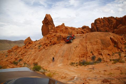 1979 Ford Bronco - A red off-road vehicle navigates a steep, rocky incline in a desert landscape. The vehicle is positioned on a narrow dirt path with large o…