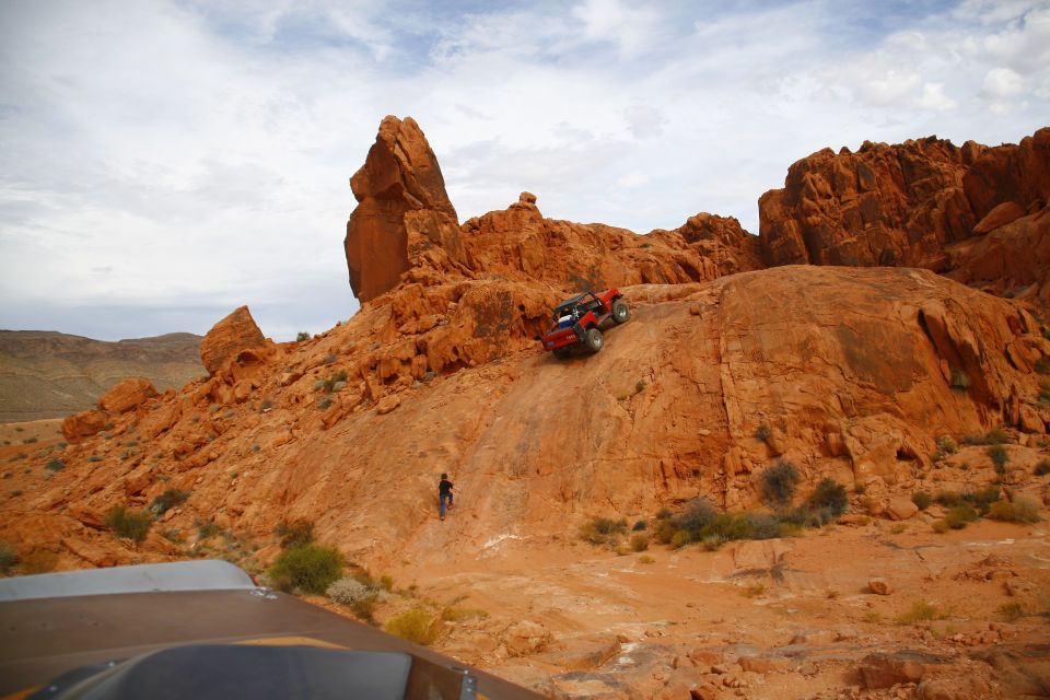 Red off-road vehicle climbing a steep rocky hill in a desert.