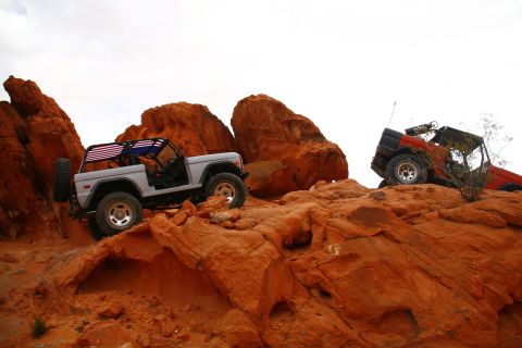 1979 Ford Bronco - Two off-road vehicles are parked on a rocky, desert landscape with red rock formations. The vehicle in the foreground is a light gray SUV w…