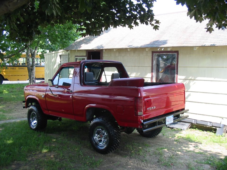 Red 1980s Ford full-size truck or Bronco with top off, lifted, in yard