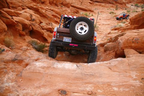 1979 Ford Bronco - A brown Ford Bronco is navigating a rocky, off-road trail in a desert landscape. The rear of the vehicle is visible, showing large off-road…