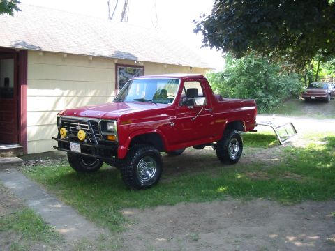 1981 Ford Bronco - This red Ford Bronco, likely from the early 1980s, features a lifted suspension, off-road lights, and chrome wheels, with its top removed.