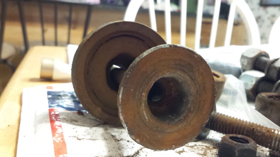 Two rusty metal circular parts with threaded holes, one larger than the other, on a table with bolts