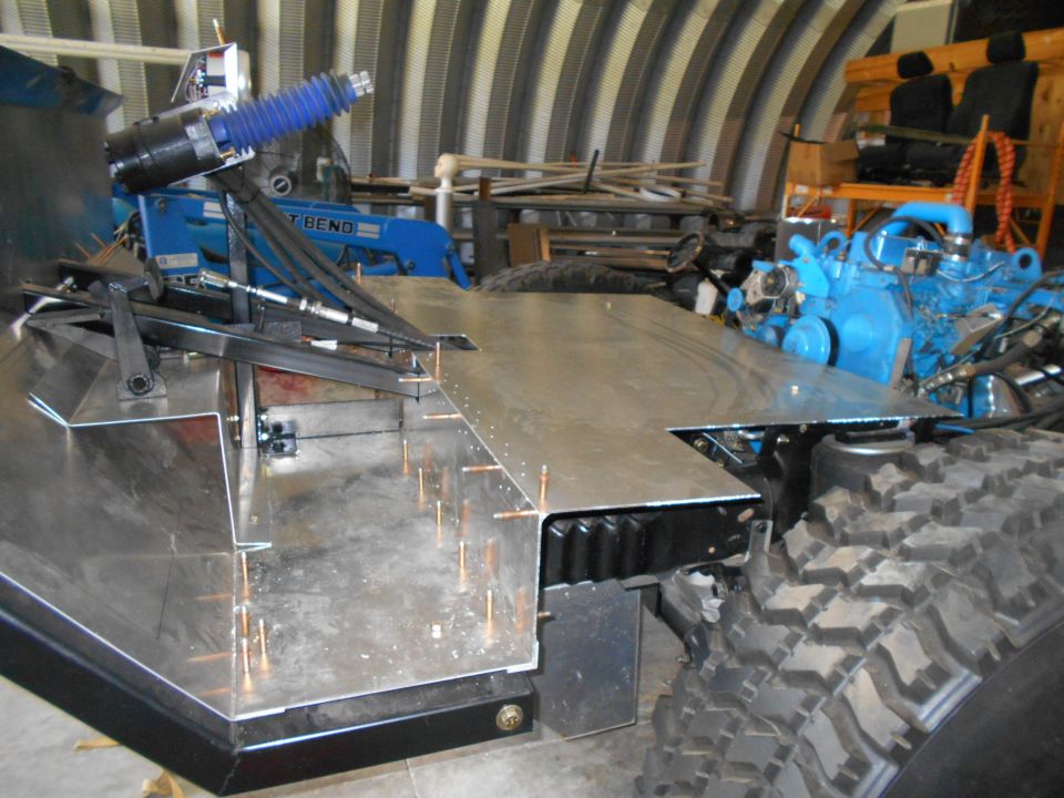Custom vehicle chassis with aluminum deck, blue engine, and large tires in a workshop.