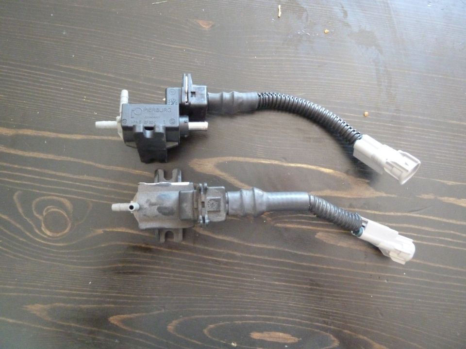 Two black electronic vacuum solenoid valves with hoses and connectors on a wooden surface.