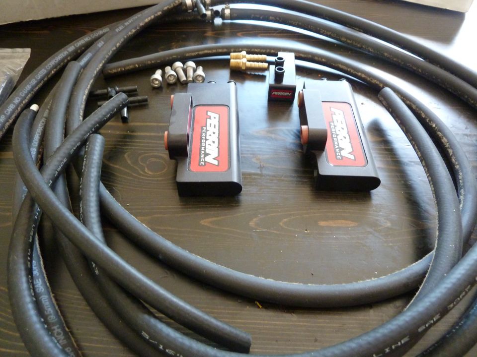 Black rubber hoses and two Perrin Performance fuel line components on a wooden table.