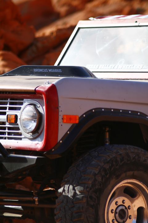 1979 Ford Bronco - Close-up of the front fender and hood of a tan and red Ford Bronco, featuring a black hood scoop with white text reading "BRONCUS MOABIUS".…