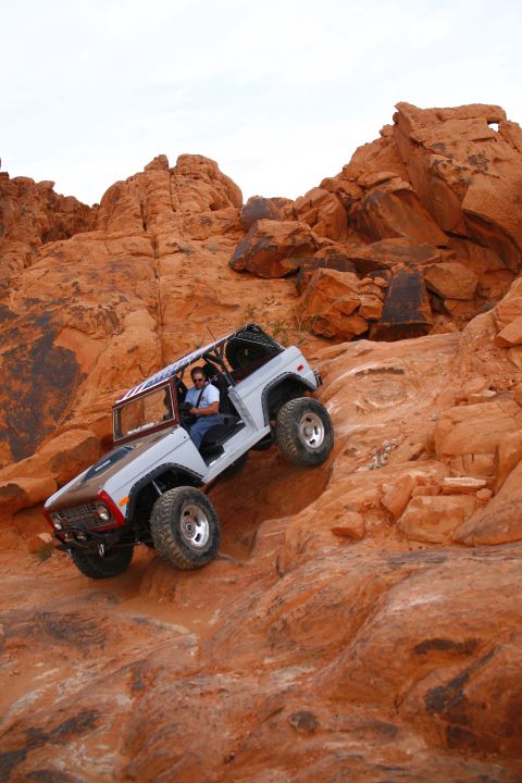 1979 Ford Bronco - A white 1979 Ford Bronco is navigating a steep, rocky, off-road trail in a desert landscape with red rock formations. The driver is visible…