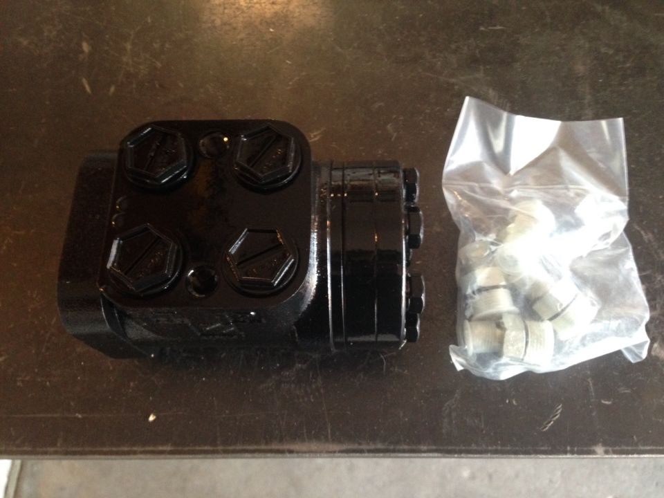 Black hydraulic steering unit with hex bolts and a bag of fittings