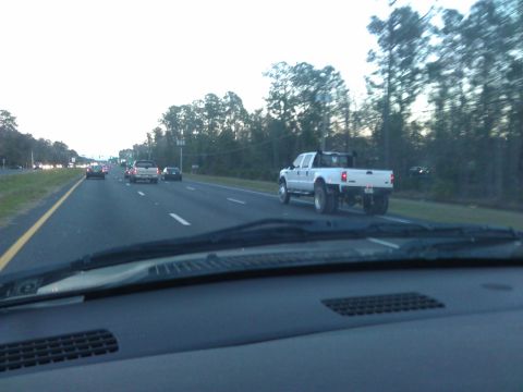 1994 Ford Bronco - A white Ford F-350 pickup truck with a dually rear axle is driving on a highway. The truck is seen from the rear passenger side, heading aw…