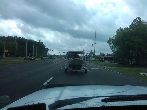 1994 Ford Bronco - A boat on a trailer is being towed down a two-lane road on a cloudy day. The trailer is attached to a vehicle that is not fully visible, bu…