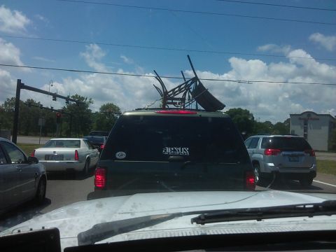 1994 Ford Bronco - A dark green SUV is seen from the rear in traffic, with a "JESUS" sticker on its back window and a "GR" sticker on the left side. The vehic…