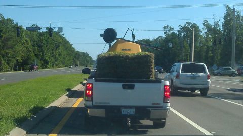 1994 Ford Bronco - A white GMC Sierra pickup truck is driving on a road, carrying a large bale of sod and a yellow piece of equipment in its bed. The truck is…