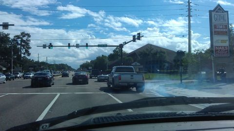 1994 Ford Bronco - A silver Ford F-Series pickup truck is seen from the rear, driving through an intersection on a cloudy day. The truck is emitting a plume o…