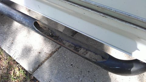 1994 Ford Bronco - A close-up view of a damaged black metal pipe, likely part of a vehicle's exhaust system, filled with dirt and debris. The pipe is situated…
