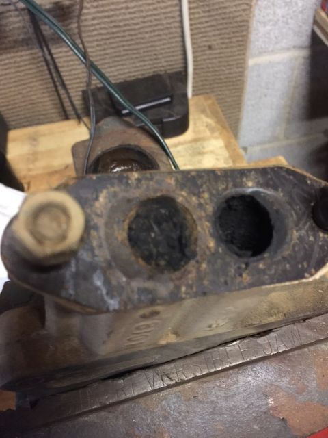1978 Ford Bronco - A close-up, angled view shows two heavily carbon-fouled exhaust ports on a metal automotive part, possibly an exhaust manifold or intake. T…