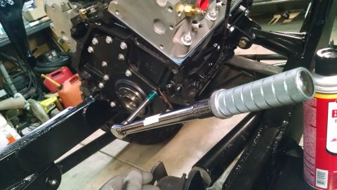 1985 Jeep CJ7 - A close-up view shows a mechanic using a torque wrench on a bolt of a black engine block. The engine appears to be part of a vehicle build,…