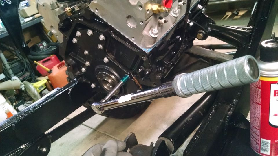 Mechanic using a torque wrench on an engine bolt, with black frame and engine parts visible.