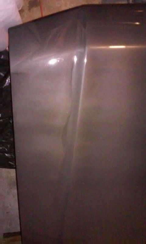 1986 Ford Bronco - A close-up view of the dark metallic paint on the side of a vehicle, showing a noticeable dent or crease running vertically down the panel.…