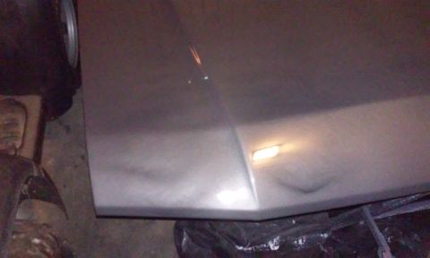 1986 Ford Bronco - A close-up, low-angle shot of a silver vehicle's hood or fender shows two significant dents. The lighting suggests the vehicle is indoors,…