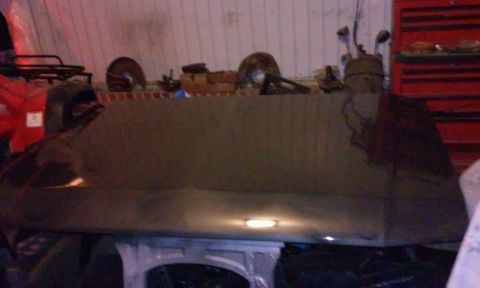 1986 Ford Bronco - A dark-colored vehicle hood is shown in a workshop setting. The hood has a glossy finish and reflects a light source from below.