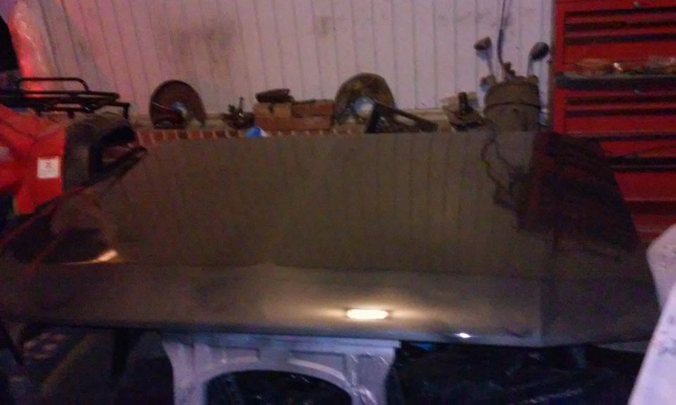 Dark glossy vehicle hood reflecting light in a workshop.