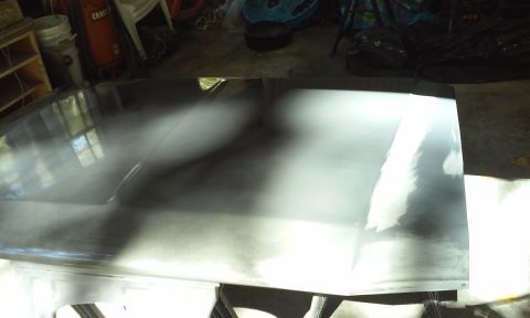 1986 Ford Bronco - The hood of a vehicle is shown in a garage setting, reflecting the surrounding environment. The surface appears to be prepped for painting,…
