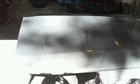 1986 Ford Bronco - A car hood is shown from a slightly elevated angle, with a light gray primer or base coat applied, indicating preparation for painting. The…