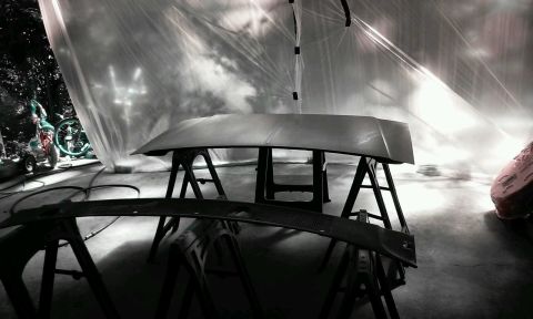 1986 Ford Bronco - A car hood and a windshield cowl are on sawhorses inside a makeshift spray booth covered with plastic sheeting. A bicycle and a small trail…