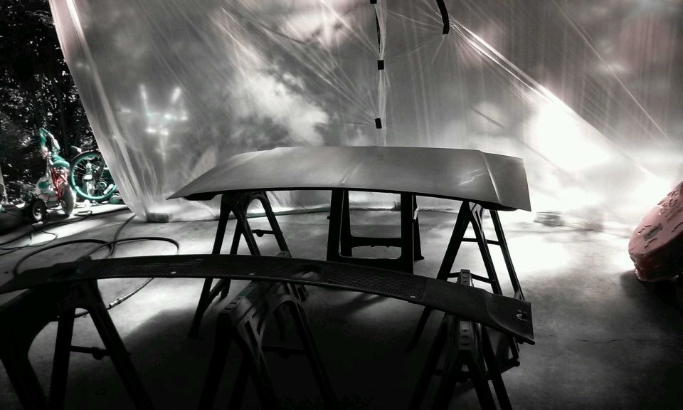 Car hood and windshield cowl on sawhorses in a spray booth.