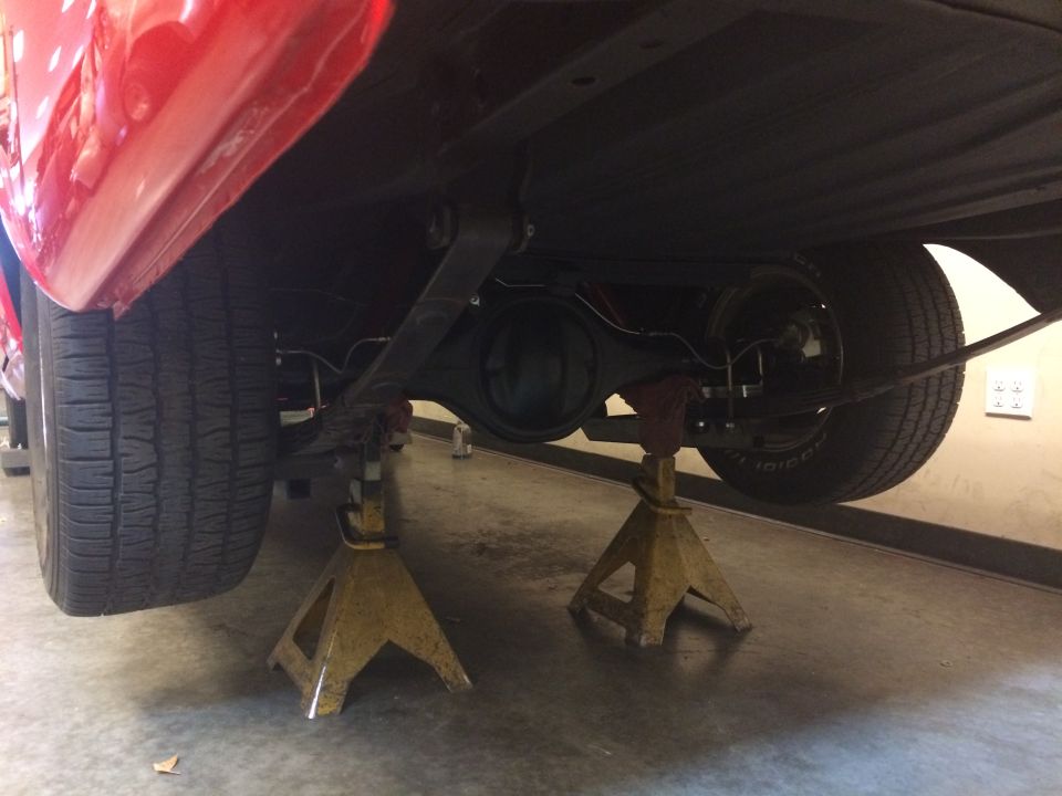 Underside of a red vehicle on jack stands, showing rear differential and tires.