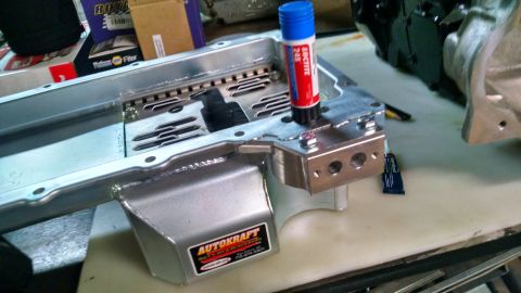 1985 Jeep CJ7 - A close-up view of a new aluminum oil pan with a Loctite applicator and a small tube of adhesive on a workbench. The oil pan has an "AUTOKR…