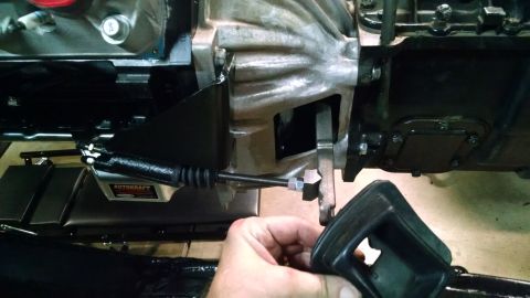 1985 Jeep CJ7 - A close-up view shows a clutch cable being attached to a manual transmission assembly. The cable has a black rubber boot and a metal adjust…