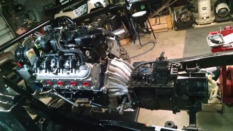 1985 Jeep CJ7 - A vehicle's engine and transmission assembly are mounted to a black frame in a garage setting. The engine appears to be a V8 with an alumin…
