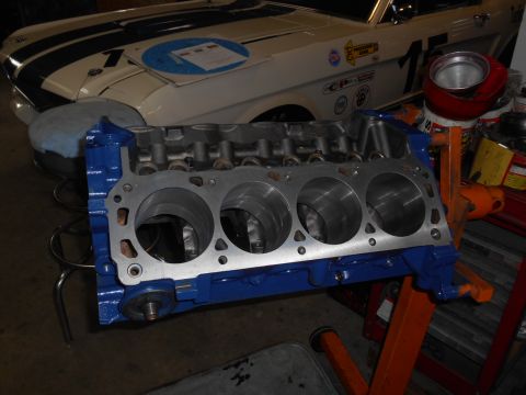 1972 Ford Bronco - A blue engine block with four cylinders is shown in the foreground, with the front end of a white classic car with blue racing stripes visi…
