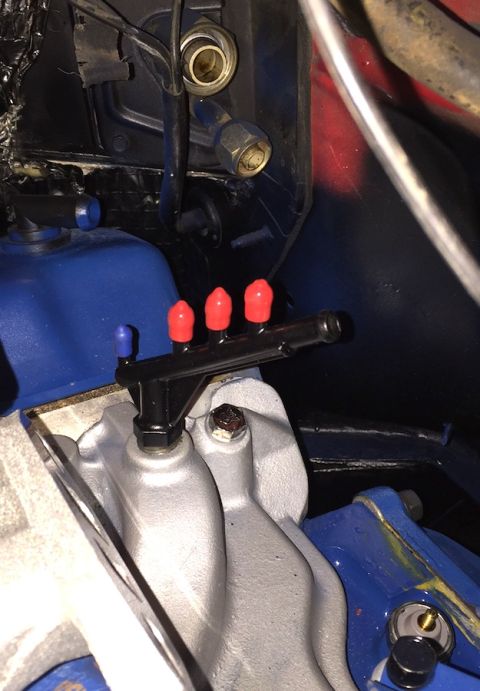 1978 Ford Bronco - A close-up view of a black fuel rail with red caps on three injectors and a blue cap on one, mounted to a silver intake manifold. The engin…
