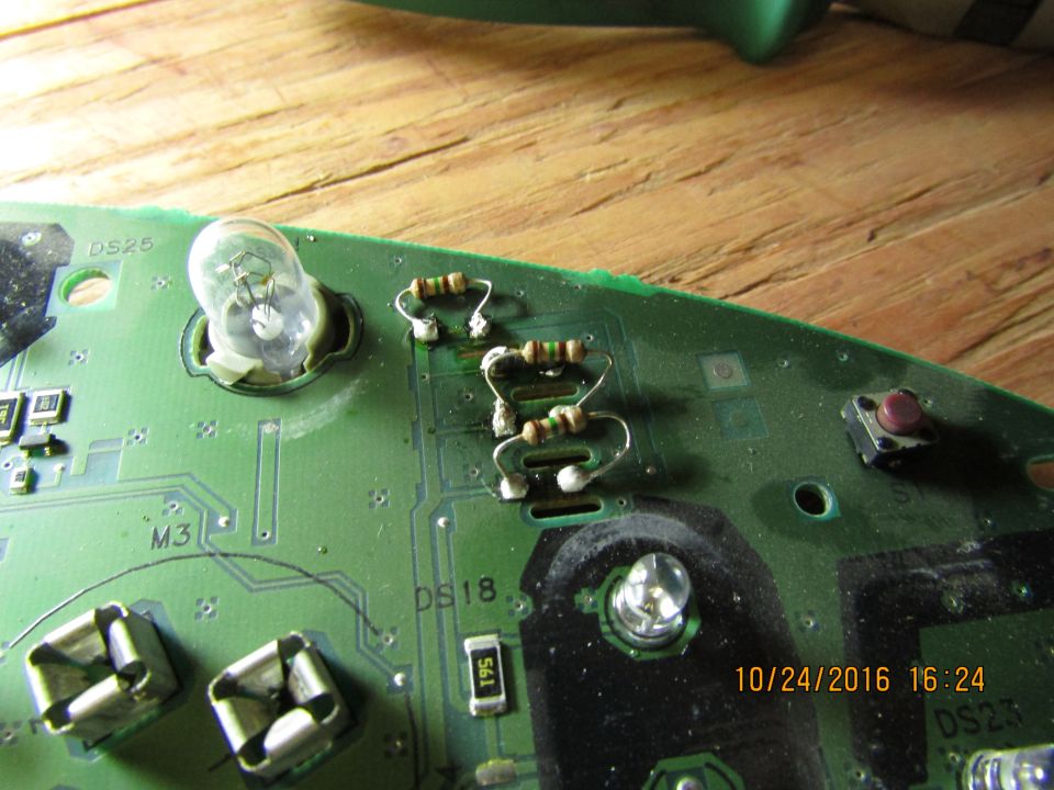 Circuit board with resistors, light bulb, and push button on a wooden surface.