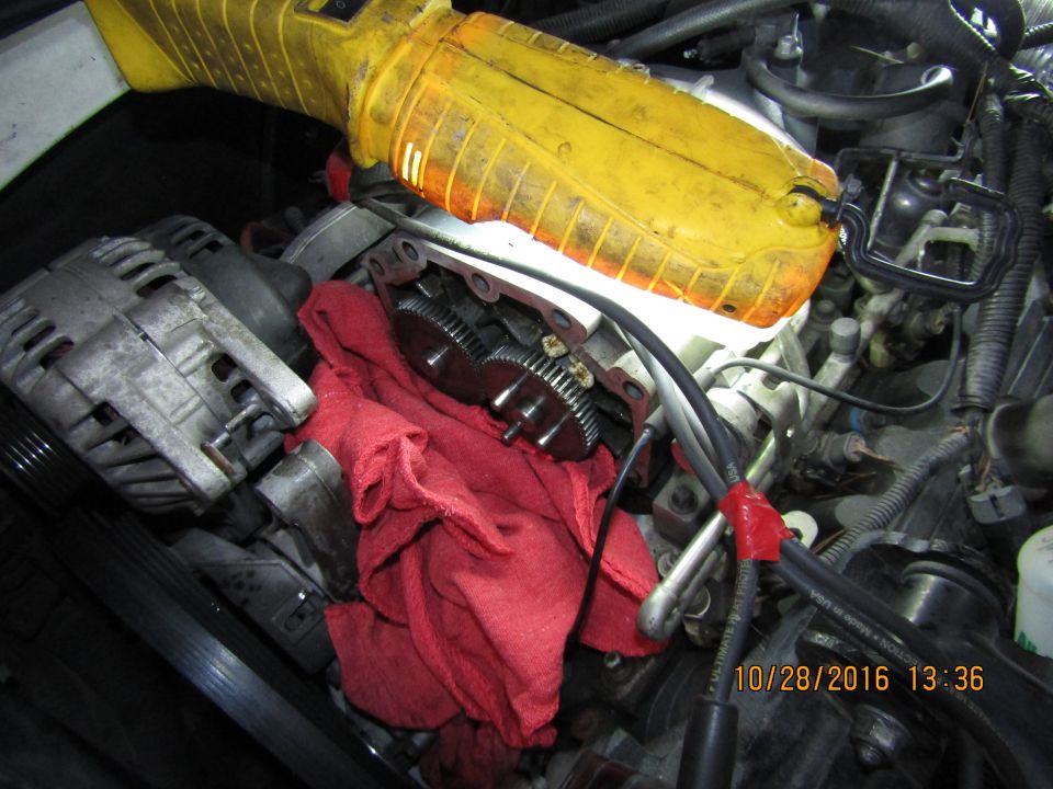 Engine bay with alternator, gears, and wiring, illuminated by a yellow work light.