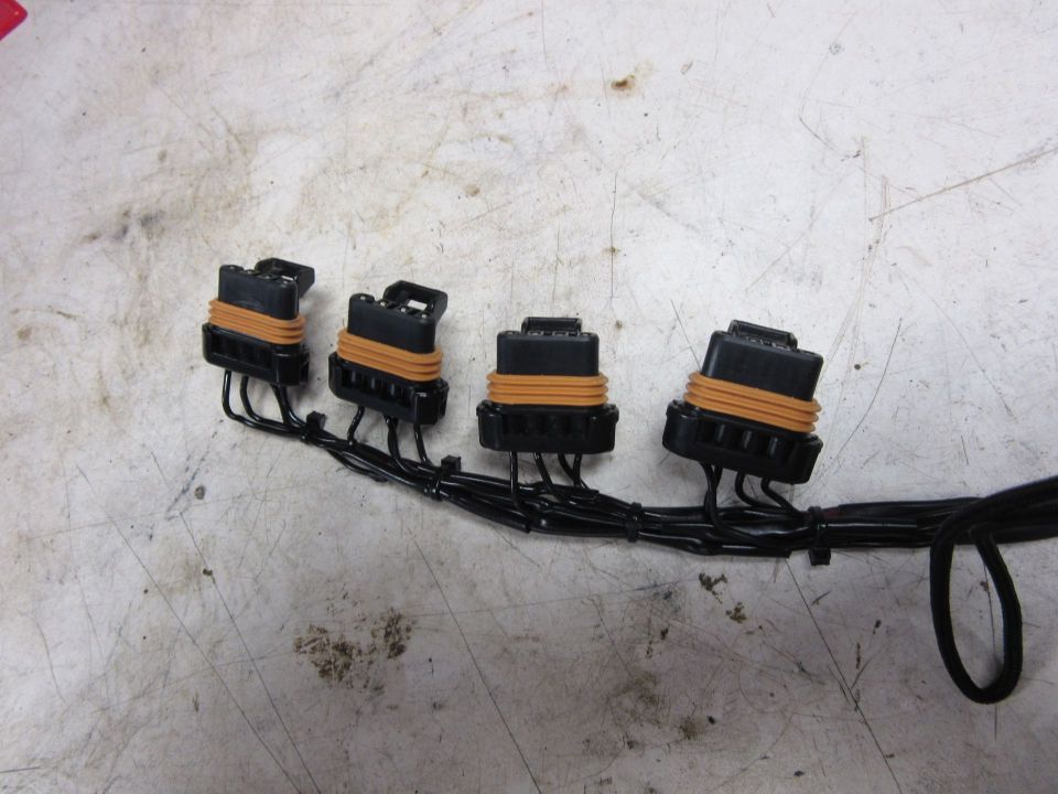 Four black electrical connectors with orange seals on a wire harness.