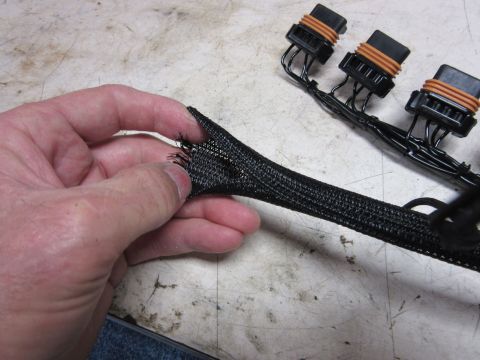 Frayed black wire loom held by a hand, with a wiring harness in the background.