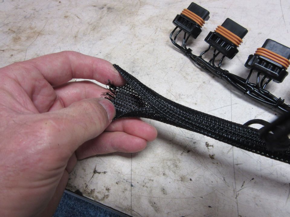 Frayed black wire loom held by a hand, with a wiring harness in the background.